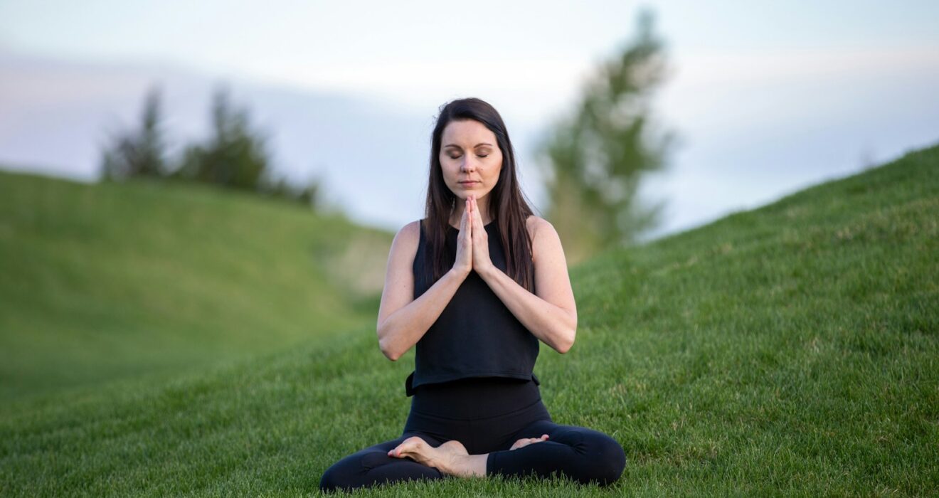 woman in black tank top and black pants sitting on green grass field during daytime