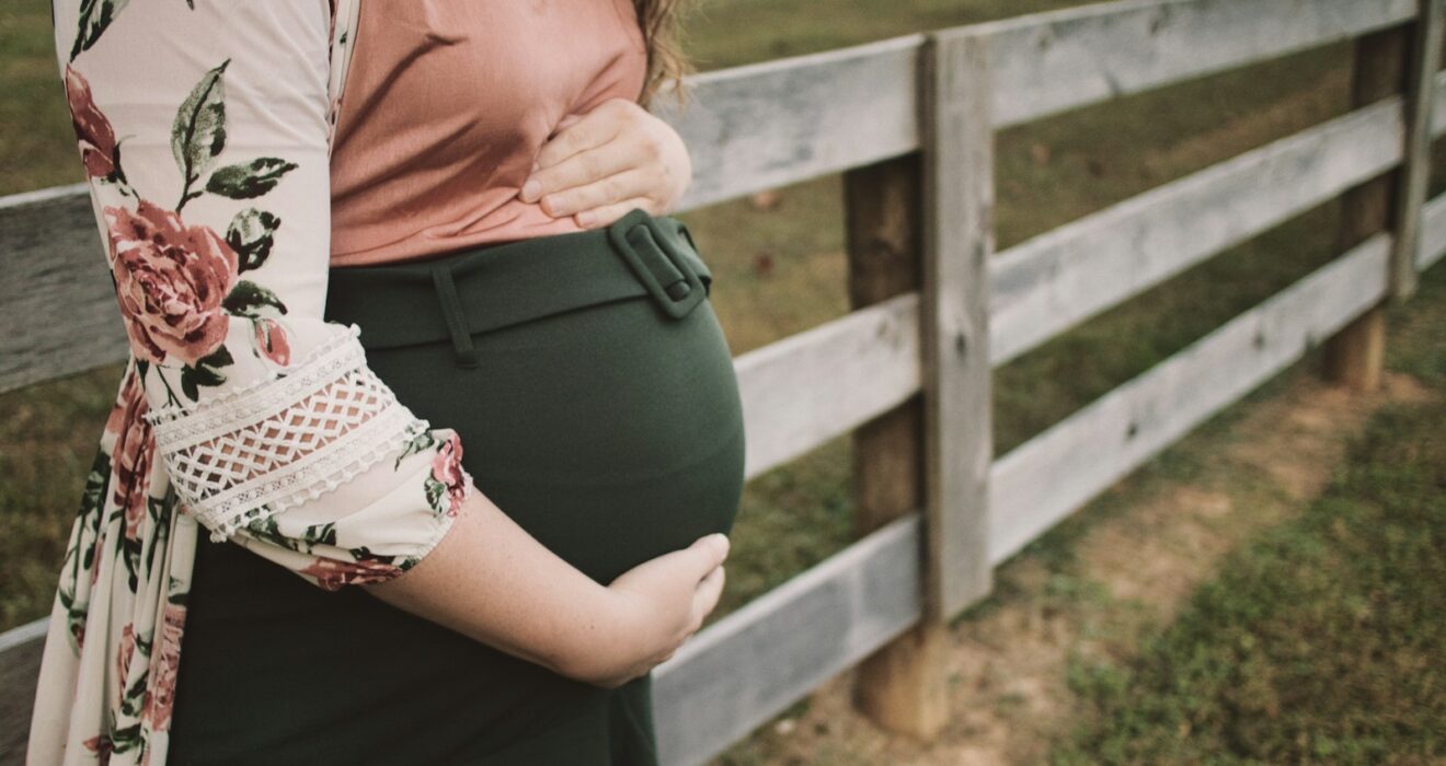 a pregnant woman standing in front of a fence