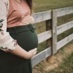 a pregnant woman standing in front of a fence
